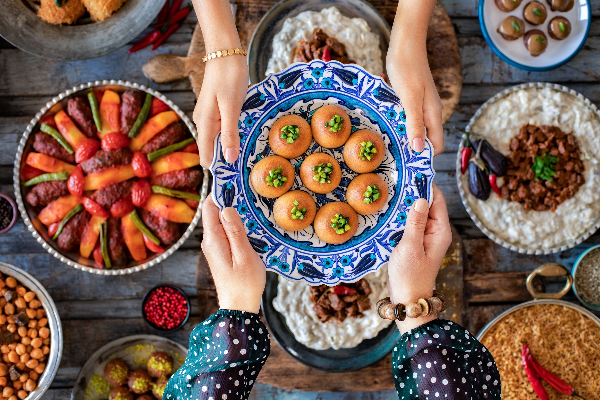Family dinner with many foods on the table and dessert at the hands of two woman. Local desserts named şekerpare and kemalpaşa tatlısı.